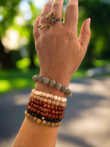 Hand wearing multiple bracelets with a laptop and colorful items in the background